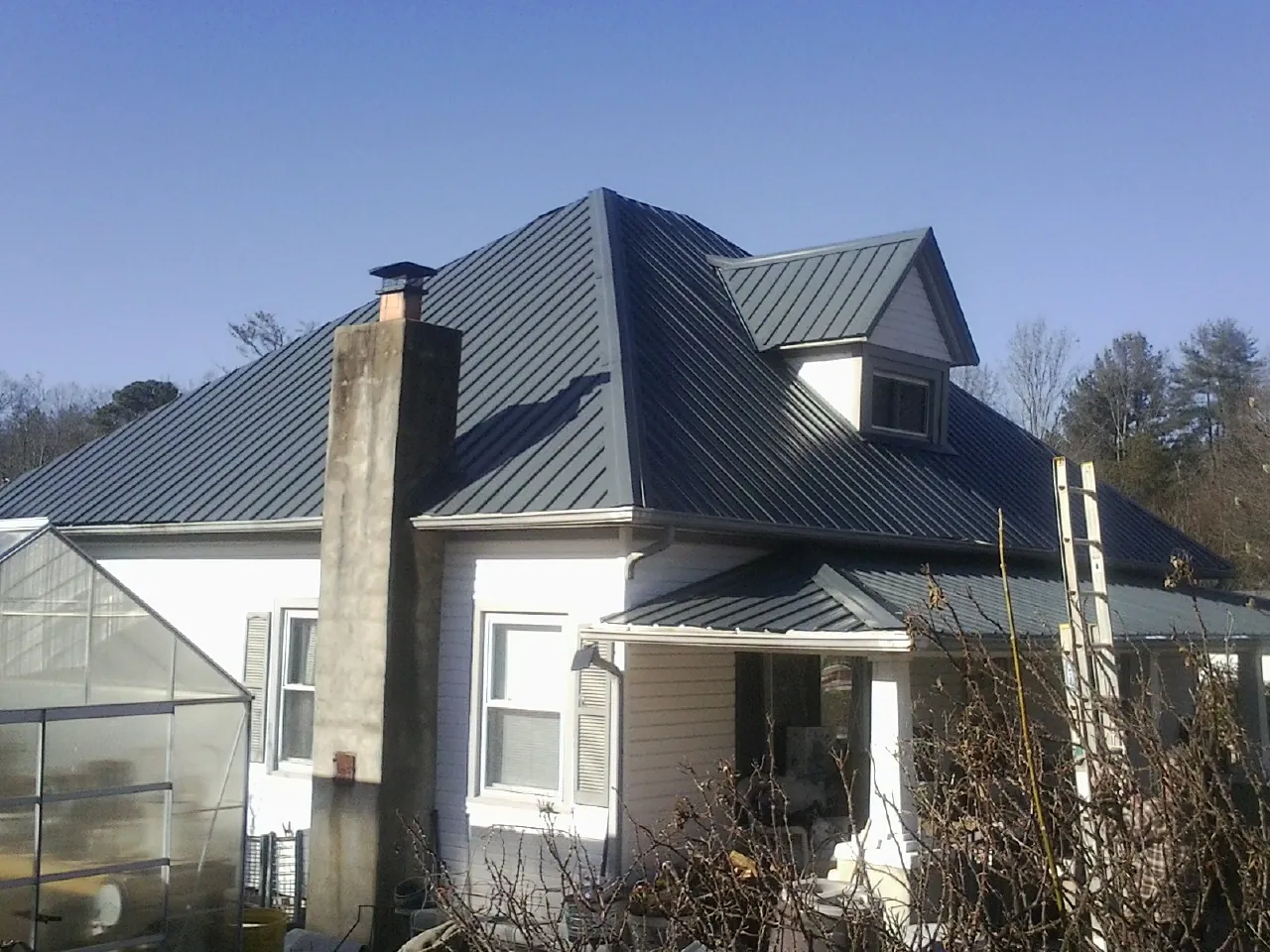 Dark blue standing seam metal roof on a white farmhouse with dormer — Slate & Tile Roof Repair by Roofing Brothers in Pinesdale