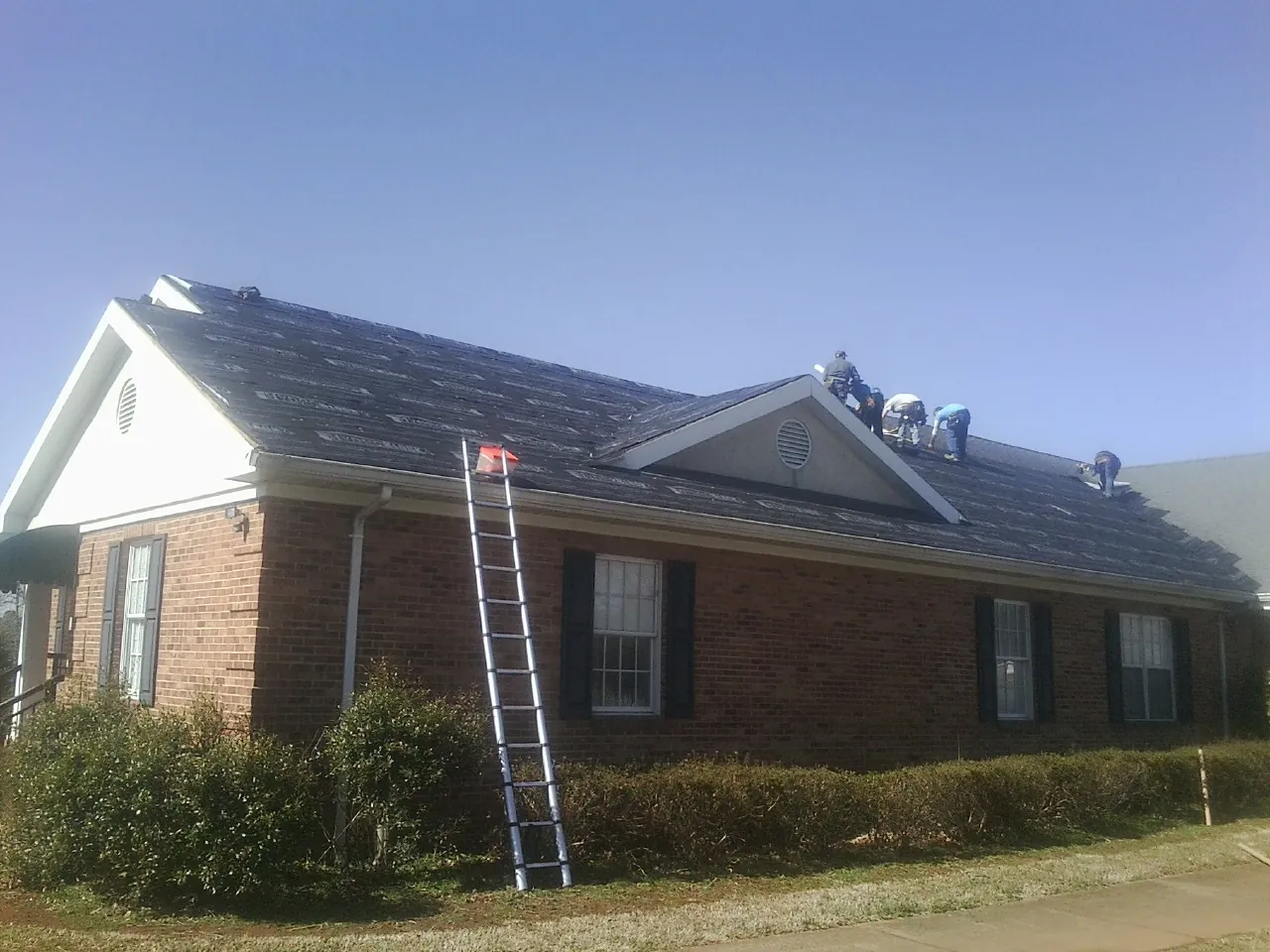 Crew tearing shingles off a brick ranch roof with a ladder set — Emergency Roof Repair work by our crew in Pinesdale