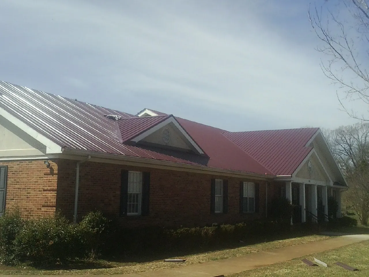 Red metal roof with gabled entries on a long brick building, from a Hail Damage Roof Repair job in Pinesdale