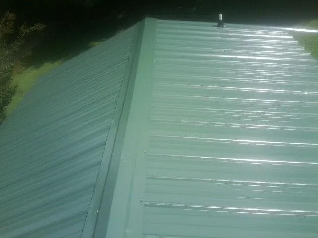 New green metal panels meeting at the ridge of a roof — Flat Roof Repair work by our crew in Pinesdale