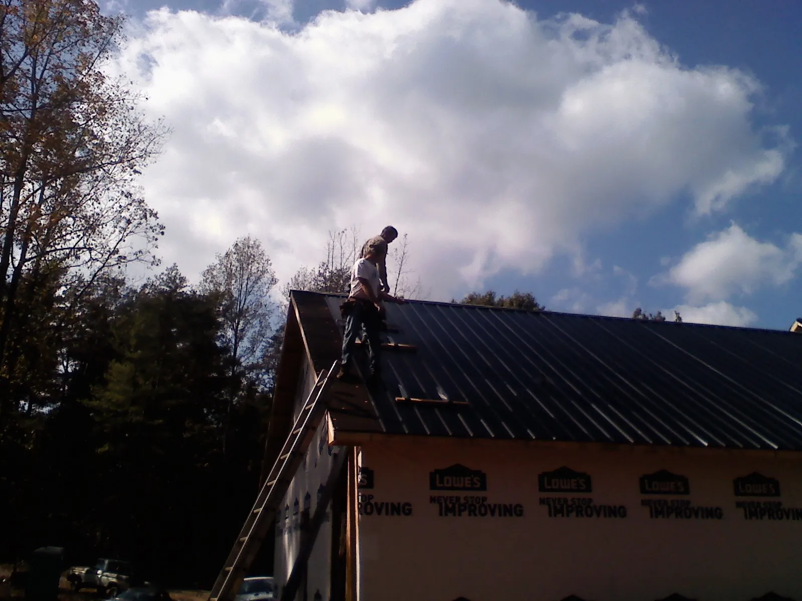 Roofer fastening dark metal panels high against a cloudy sky, from a Roof Inspection job in Pinesdale