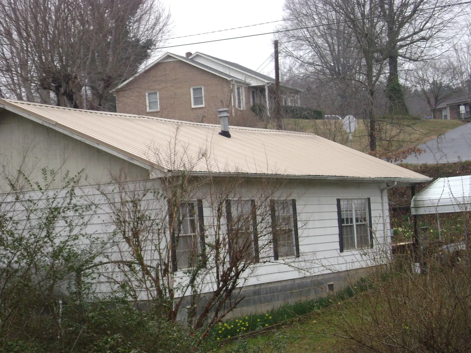 Tan metal roof on a white sided house set into a hillside — Commercial Roofing by Roofing Brothers in Pinesdale